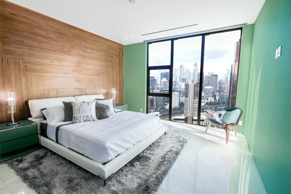 Planning a Trip to Melbourne. Modern and contemporary bedroom in Melbourne with views of the financial district of the city. Condo or Hotel accommodation. Pale green, maple and gray colors.