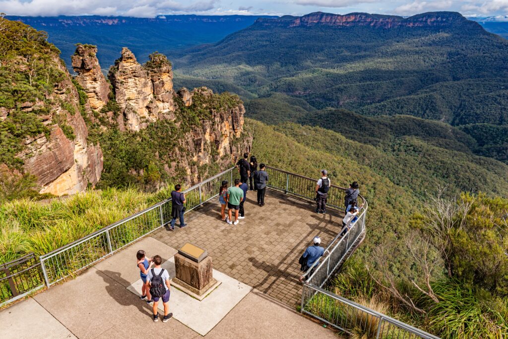 Tourists enjoy the view of the “Three Sisters” rock formation in the Blue Mountains National Park near Katoomba, NSW, Australia 