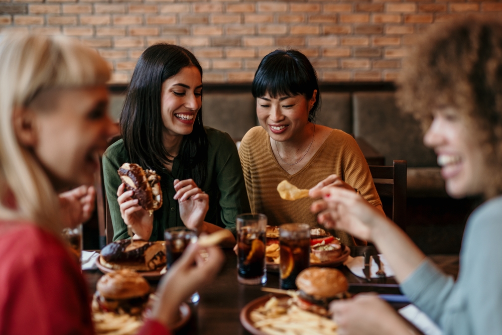 Young happy people having lunch together. Focus on a smiling females talking and grabbing a chips 