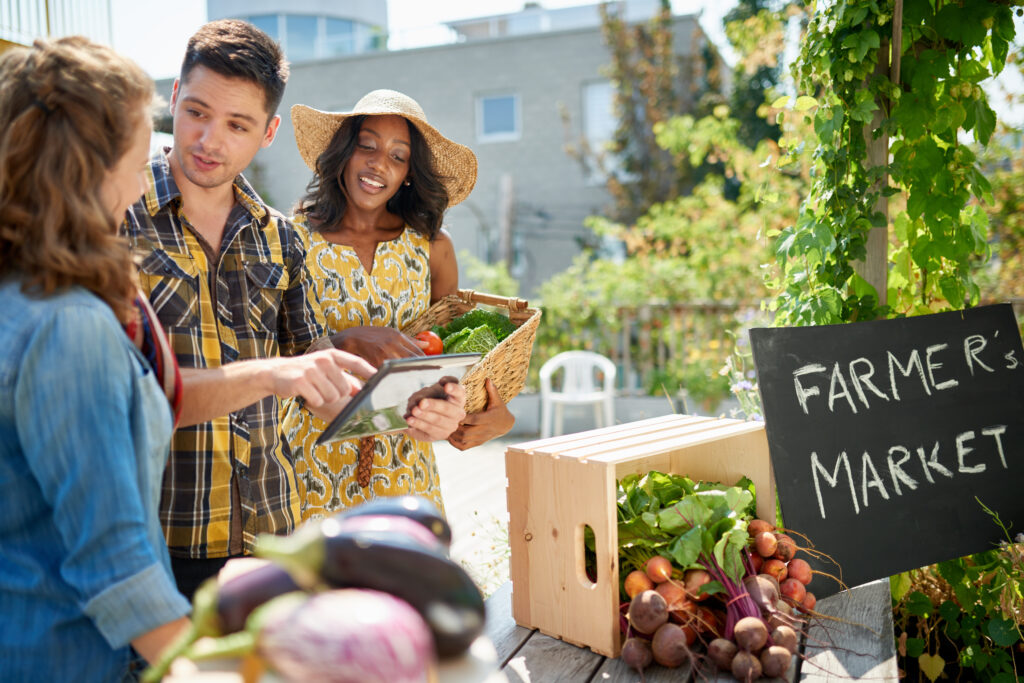 Friendly woman tending an organic vegetable stall at a farmer's market and selling fresh vegetables from the rooftop garden