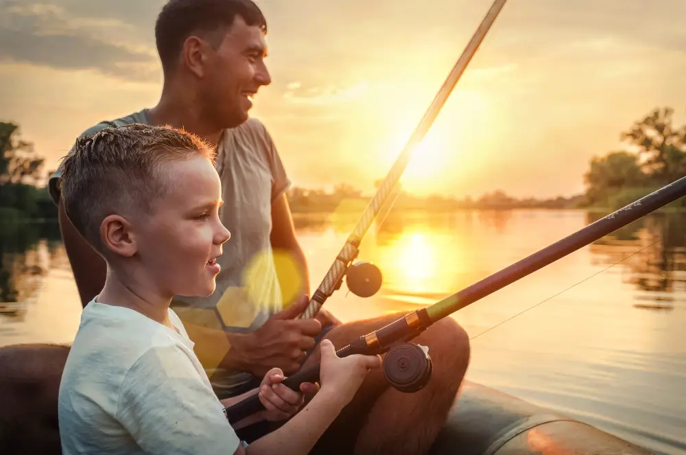 Glen Riddle Recreation Reserve. Happy Father and Son together fishing from a boat at sunset time in summer day under beautiful sky on the lake.