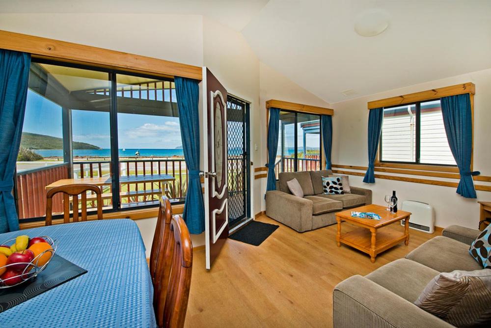 The inside of a cabin looking out past the dining table and lounge room toward the ocean at Acclaim Rose Gardens Beachside Holiday Park