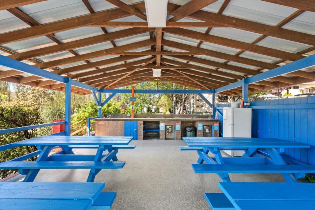 A covered BBQ area with blue tables and chairs for families to enjoy breakfasts, lunches or dinners