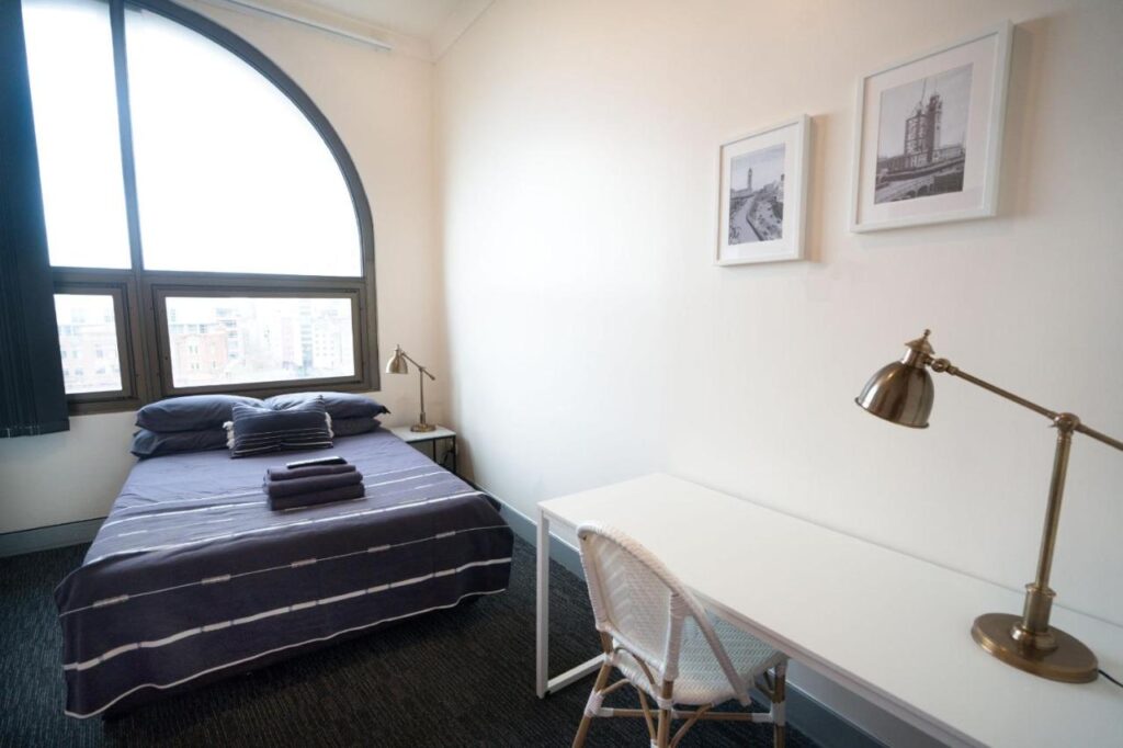 A private room with desk and queen bed and a large arch window with views of Sydney at Hostel Wake Up! Sydney Central