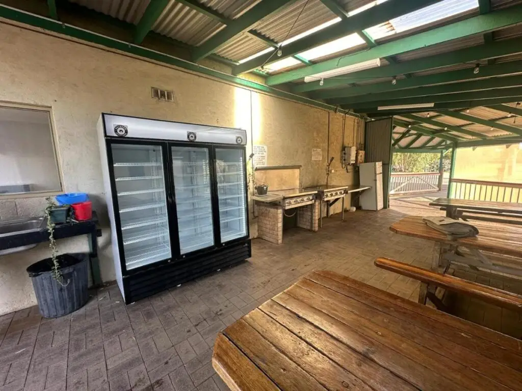 A BBQ area with wooden seating, under a cover for guests to socialise at Kalbarri Backpackers Hostel