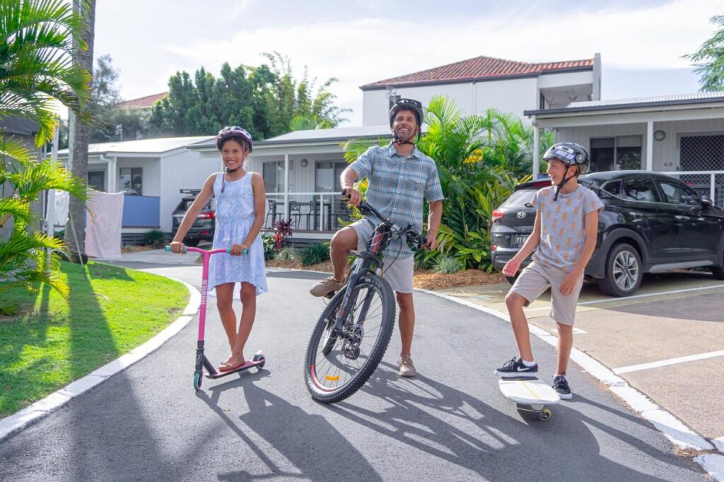 A dad and his kids ready for activities, riding a bike, skooter and skateboard at Nobby Beach Holiday Village