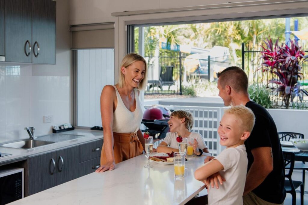 A happy family having a refreshing drink and a snack in the kitchon of one of the cabins at Nobby Beach Holiday Village