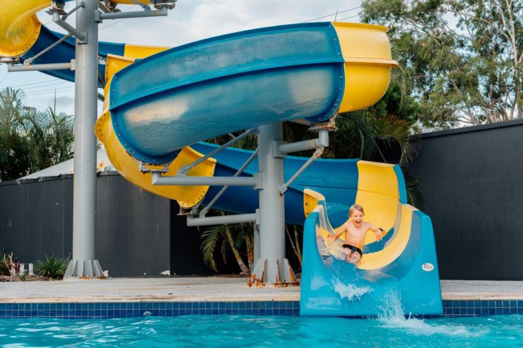 A kid having fun sliding down a blue and yellow water slide. 