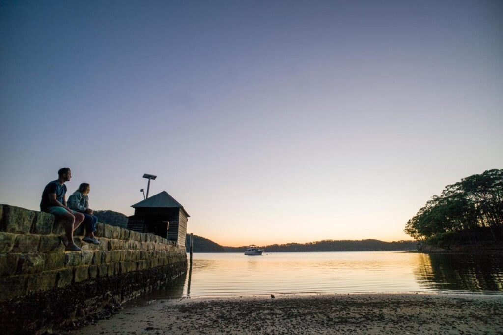 Travelers sitting by the water as the sun sets at YHA Pittwater Eco Sydney