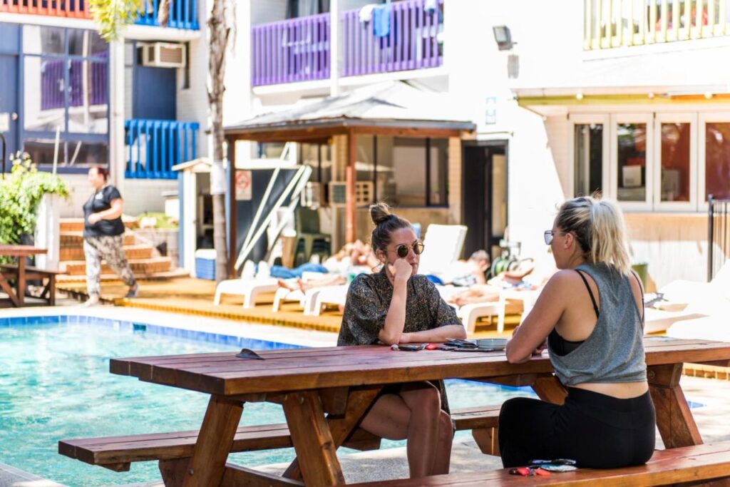 A couple of travellers having a chat under the shade of a tropical tree next to the pool at Billabong Backpackers Resort