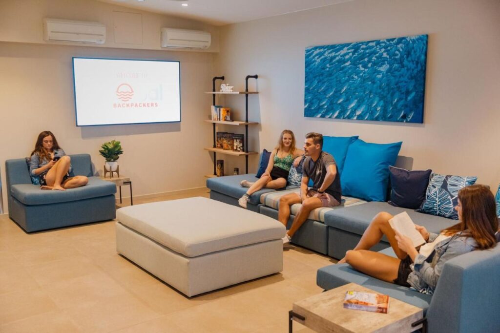 A clean comfy loung room with big screen television and cosy lounges with travellers relaxing at Global Backpackers Cairns