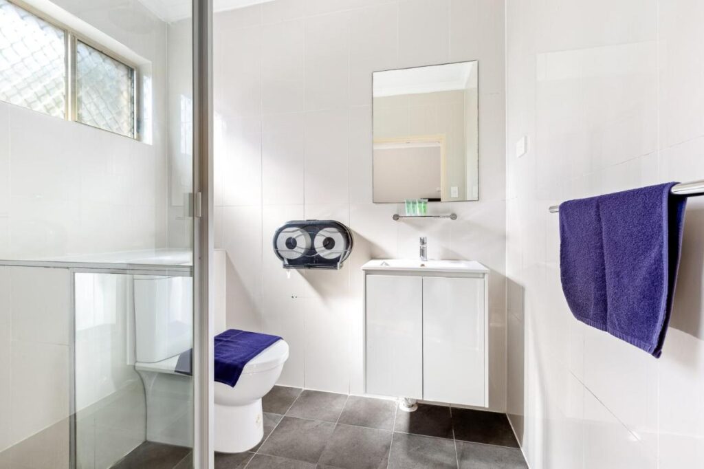 Clean and well maintained bathroom with shower, toilet and sink and a mirror at Newtown Backpackers