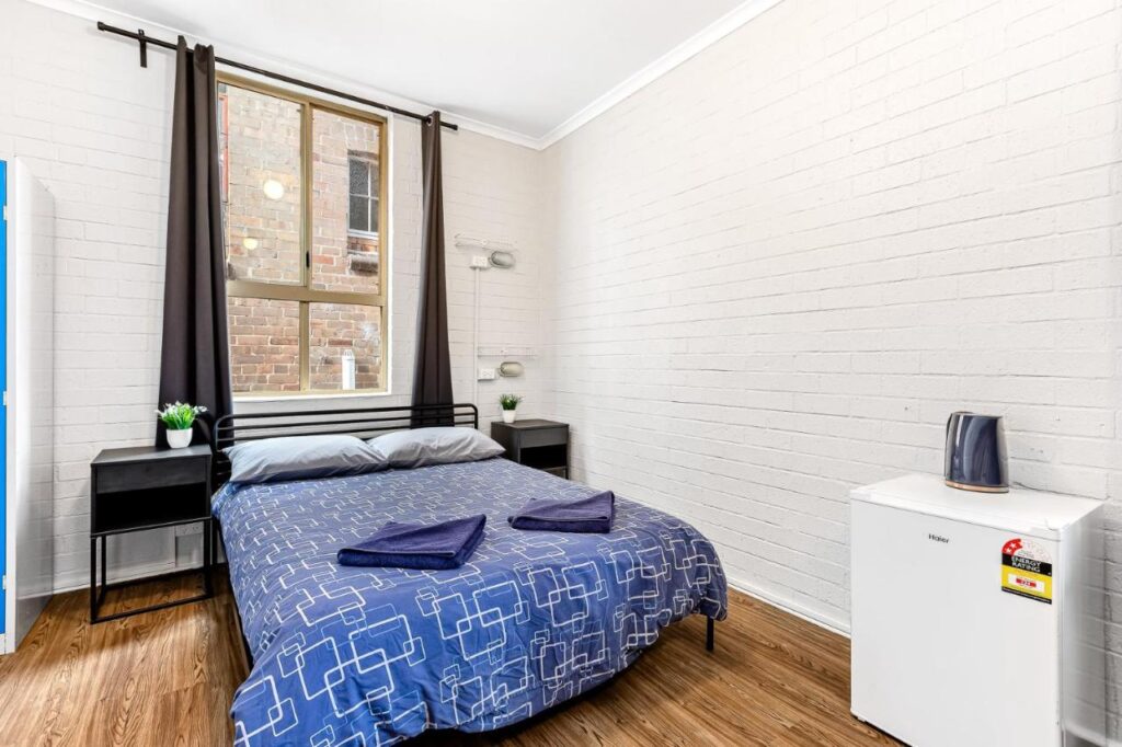 A private room with queen sized bed, refrigerator and a large window at Newtown Backpackers