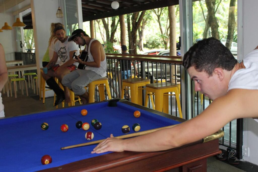 A traveller playing a game of pool in the bar area and other travellers chatting in the background at Port Douglas Backpackers