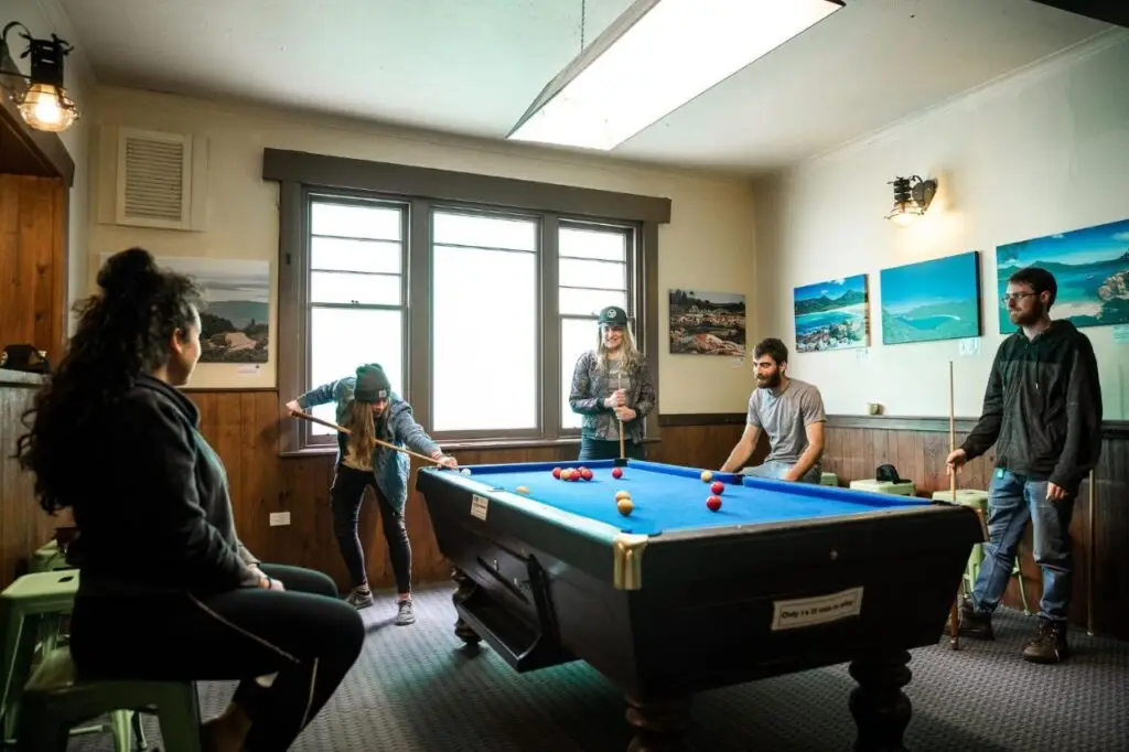 The games room with travellers playing a game of pool at The Pickled Frog Hostel.