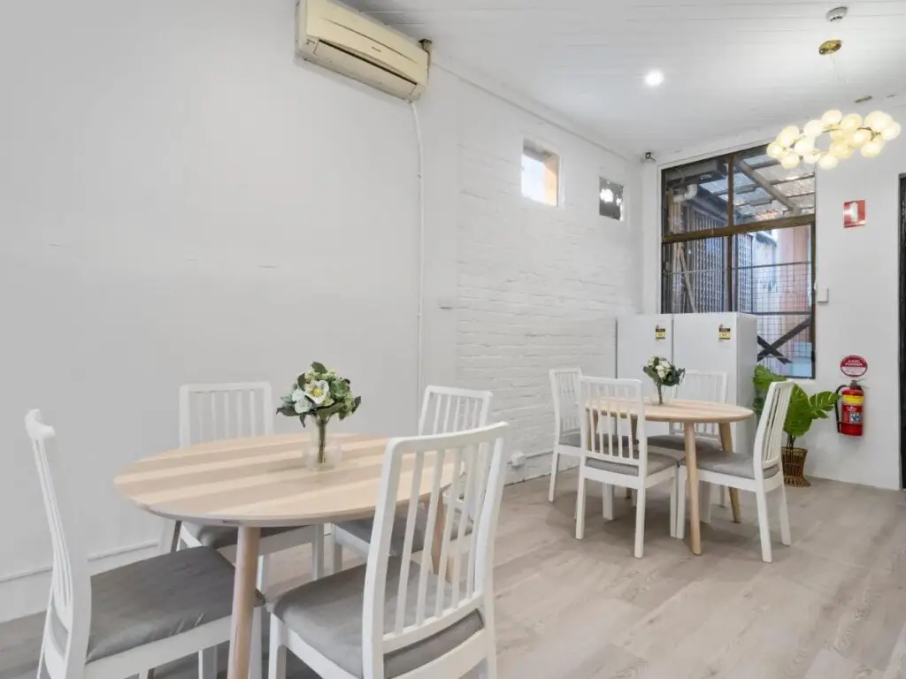 A modern designed kitched with round tables and light wooden  tops, white chars and a vase with flowers at Urban Nomad Potts Point