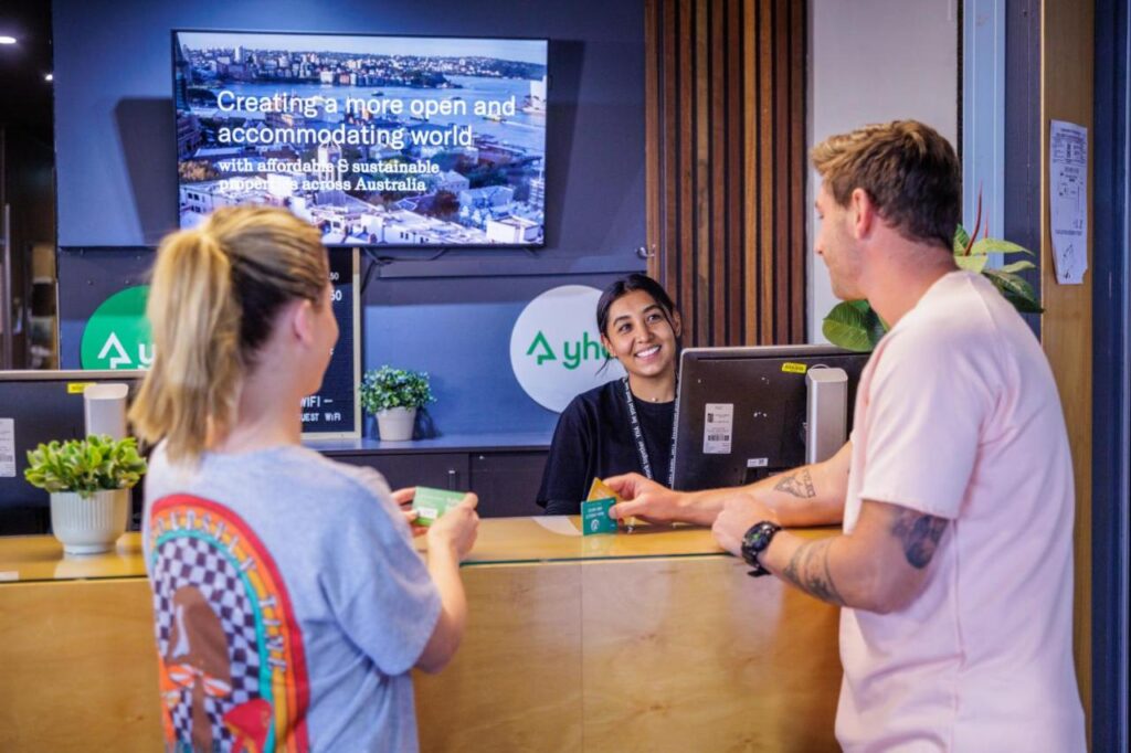 A couple of travellers checking in with the help of a friendly staff member at YHA Melbourne Central