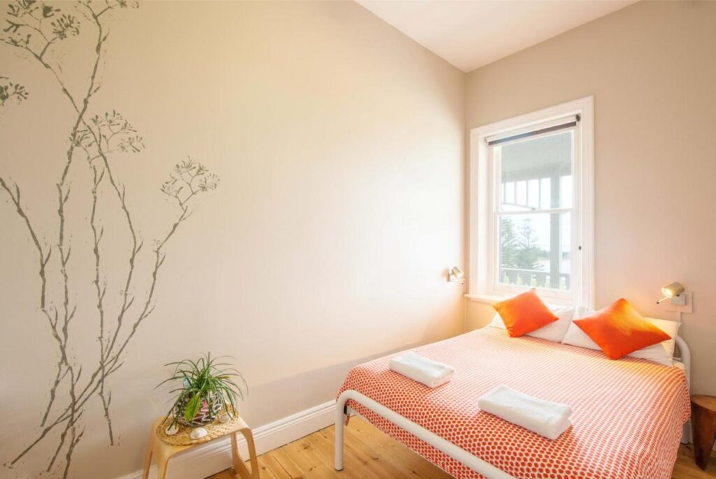 A private room with queen bed side table and a pot plant with a large window at YHA Port Elliot Beach House